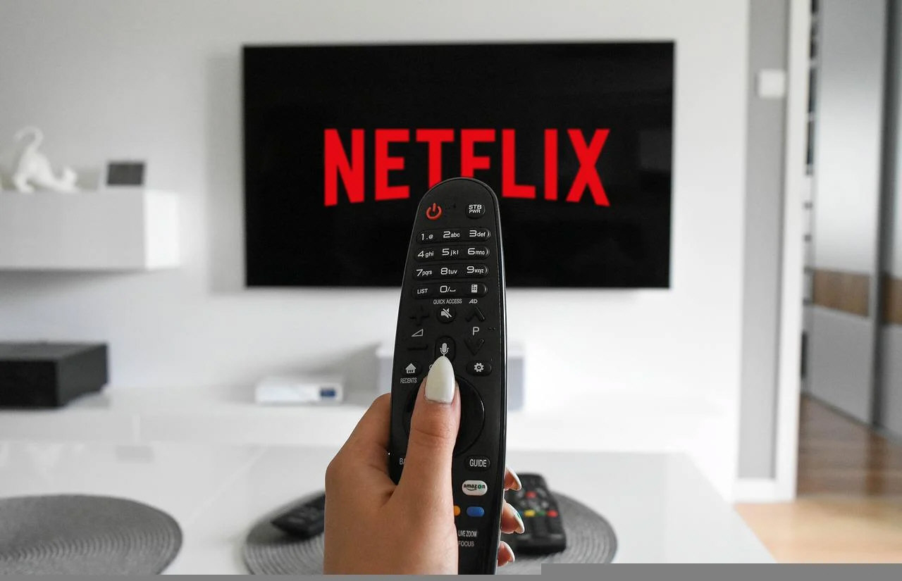 Mão de uma mulher segurando um controle remoto e apontando para uma televisão com o logotipo da Netflix