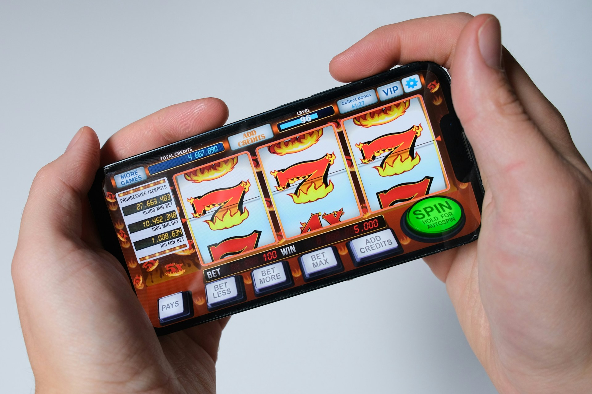 Pessoa utilizando um smartphone para jogar em um aplicativo de caça-níqueis, com a tela exibindo símbolos coloridos típicos de jogos de cassino.